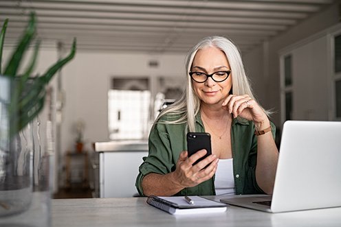 senior female at laptop looking at phone